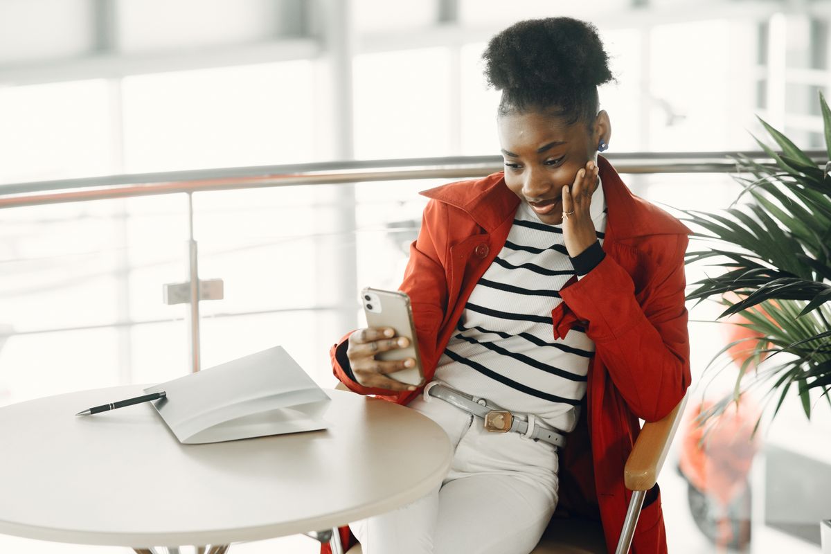 Une jeune femme en veste rouge sourit en lisant un message sur son téléphone