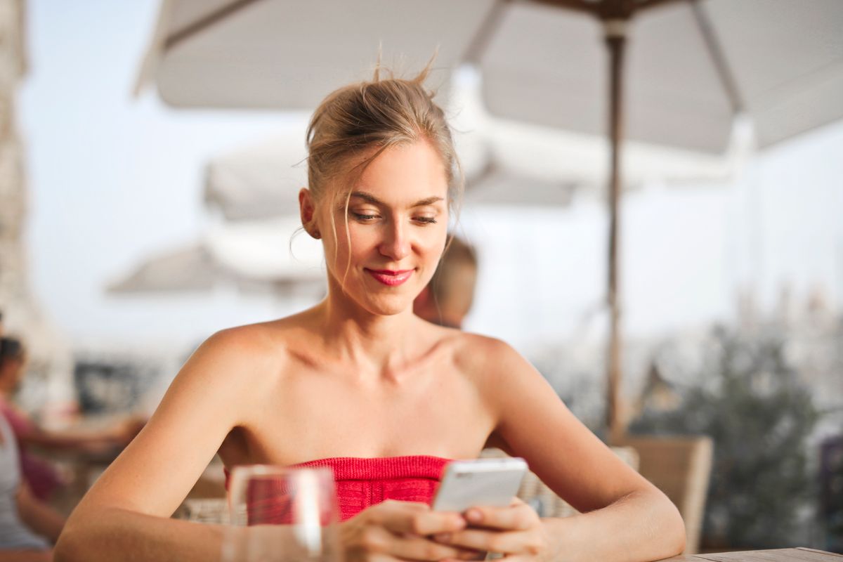 Une femme souriante utilise son téléphone à la terrasse d’un café