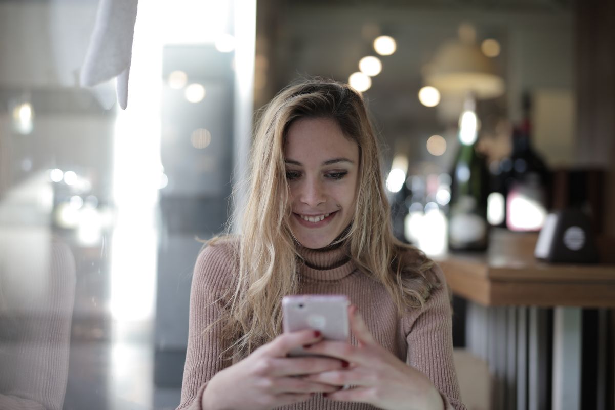En kvinde smiler, mens hun kigger på sin telefon